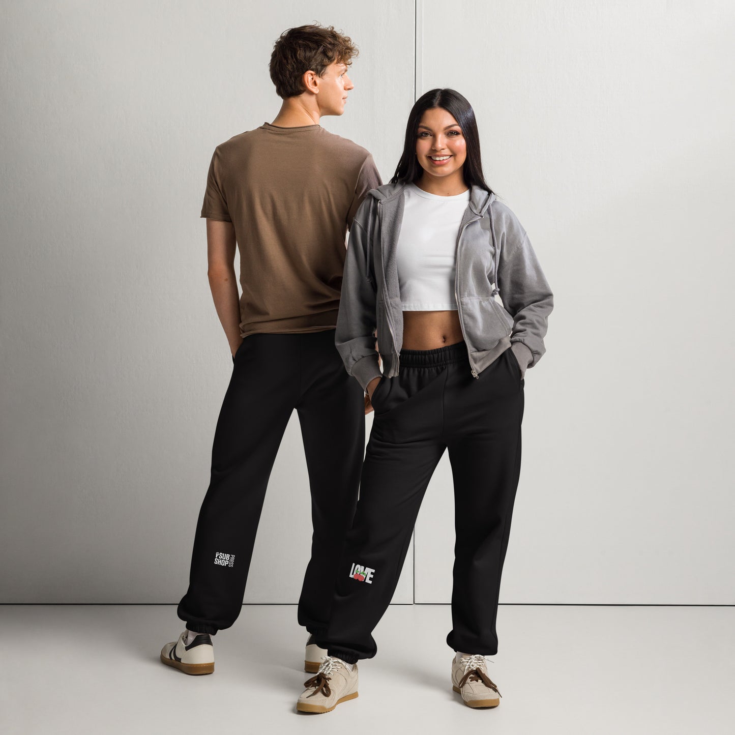 Two people wearing matching black pants with logos, standing against a plain background.