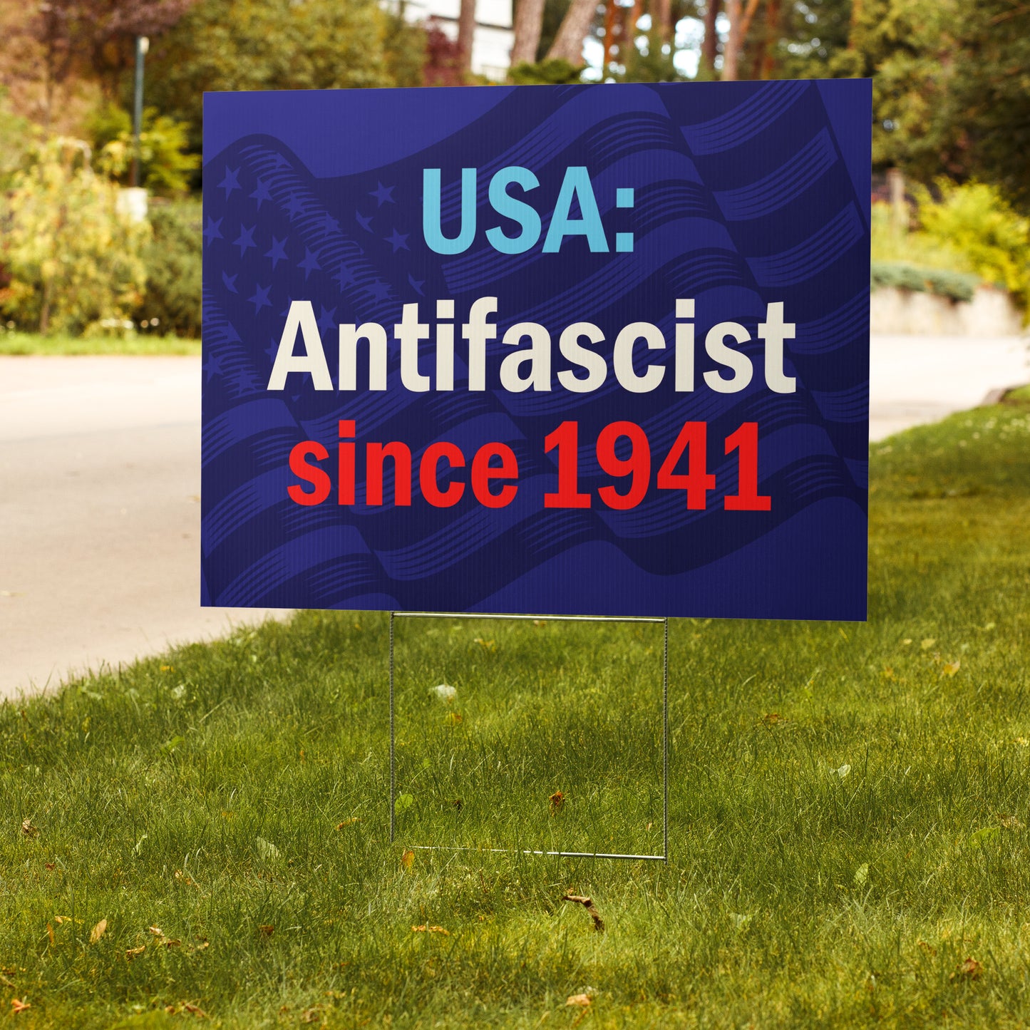 Garden sign with 'USA: Antifascist since 1941' text on a blue background with waving flag pattern, placed outdoors.
