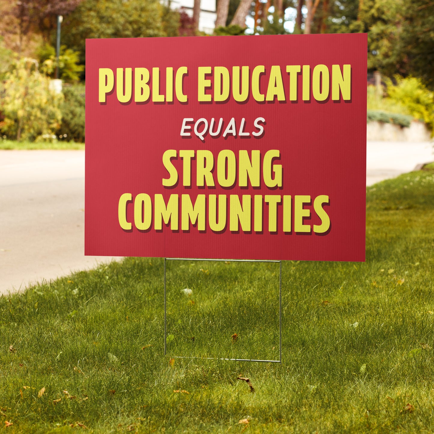 Red sign with yellow text 'PUBLIC EDUCATION EQUALS STRONG COMMUNITIES' on a grassy lawn.