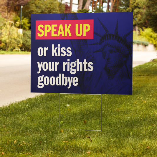 Yard sign with text 'Speak Up or kiss your rights goodbye' in front of a blurred natural background.